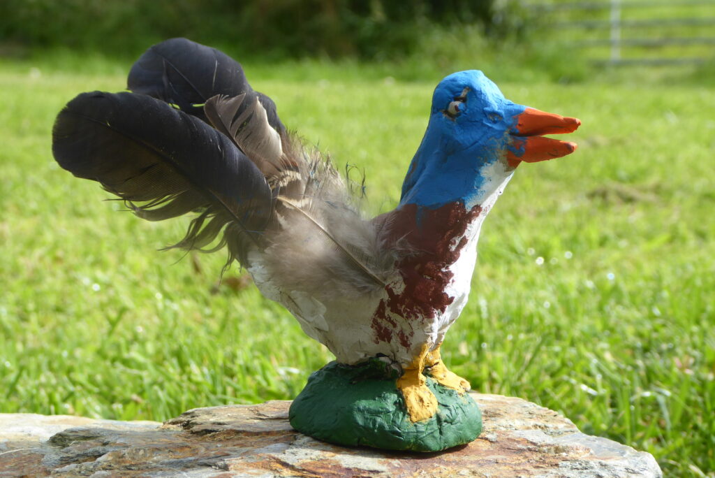 A clay bird that has been painted with a feathered tail