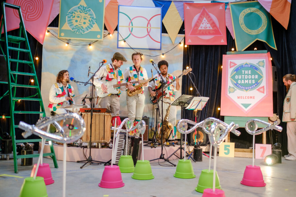 A band in colourful waistcoats plays in front of some up turned plant pots coloured green and pink.