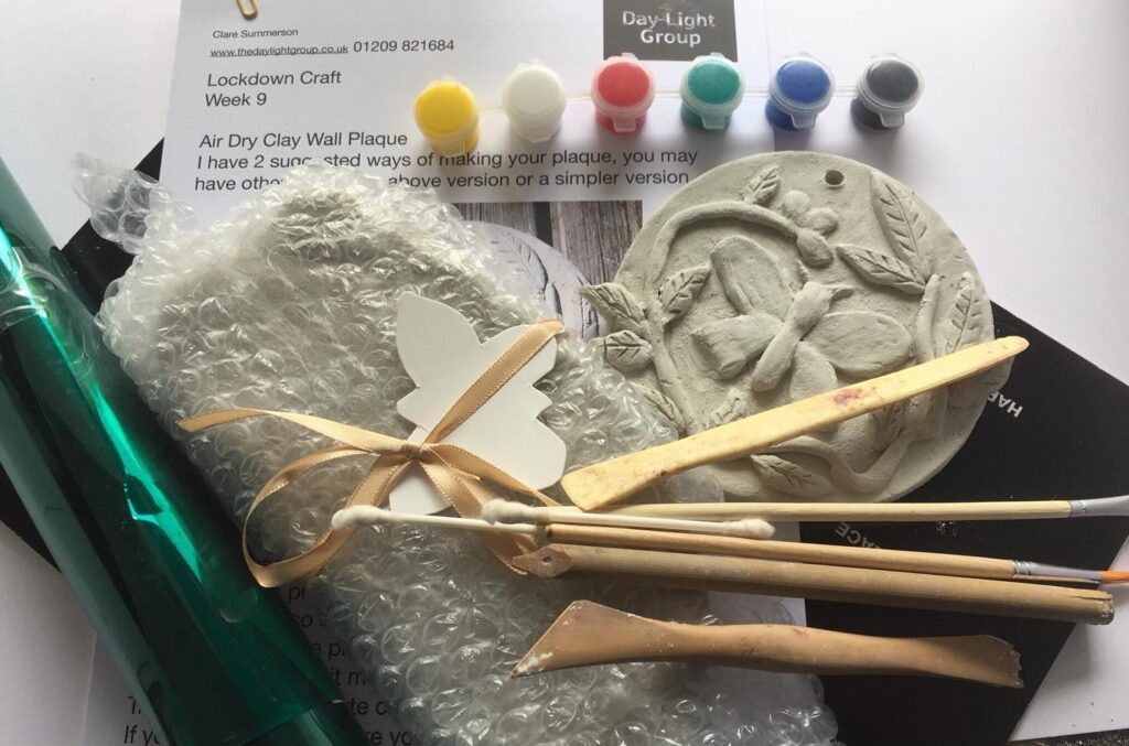 A craft pack containing little pots of paint, wooden tools, and a clay wall plaque.